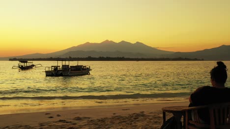 A-woman-relaxing-on-a-chair-taking-photos-of-the-beautiful-golden-sunset-over-the-ocean