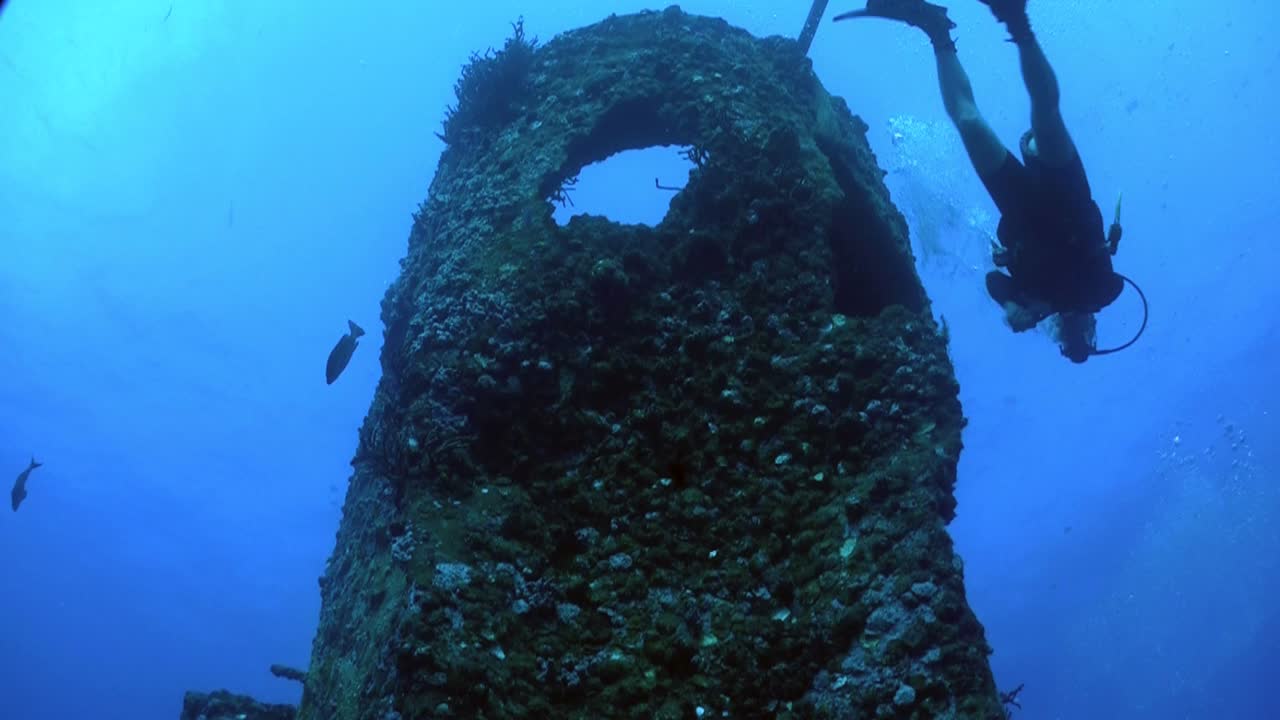 잠수부가 낮은 각도에서 난파선 주위를 헤엄치고 있다