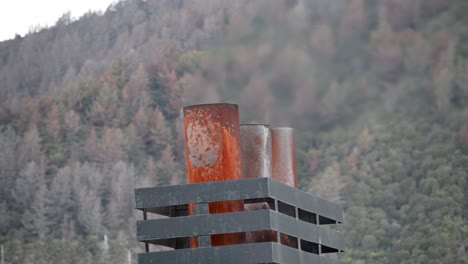 rusty exhausts of a ferry ship letting out hot, shimmering gas, isolated in front of coastal mountains covered with coniferous forests