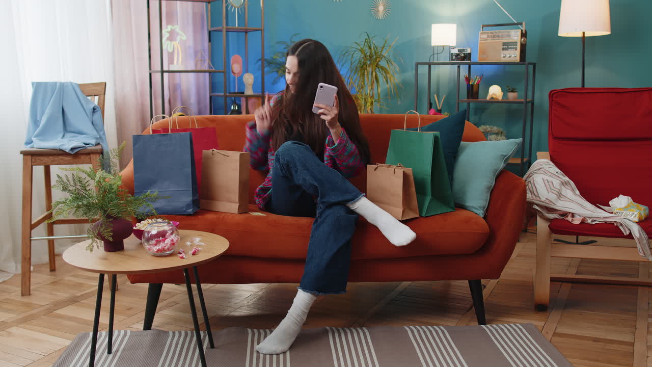 Happy shopaholic young woman sitting with shopping bags making online payment with credit card home