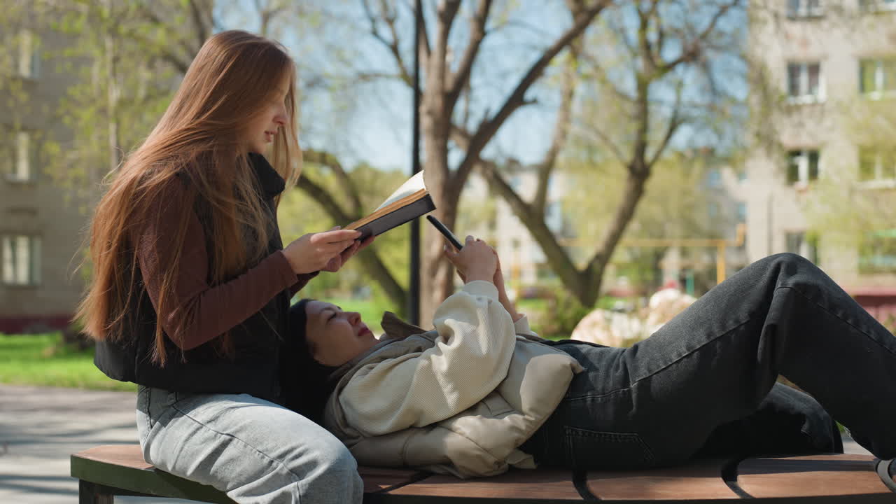 ragazze adolescenti che si godono una lettura rilassante, giovani donne sedute insieme che si godono un momento di lettura tranquillo, ragazze adolescenti di diversa provenienza che leggono insieme all'aperto durante la primavera
