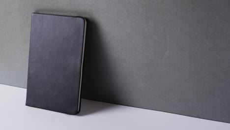 close up of closed black book leaning on wall with copy space on gray background in slow motion
