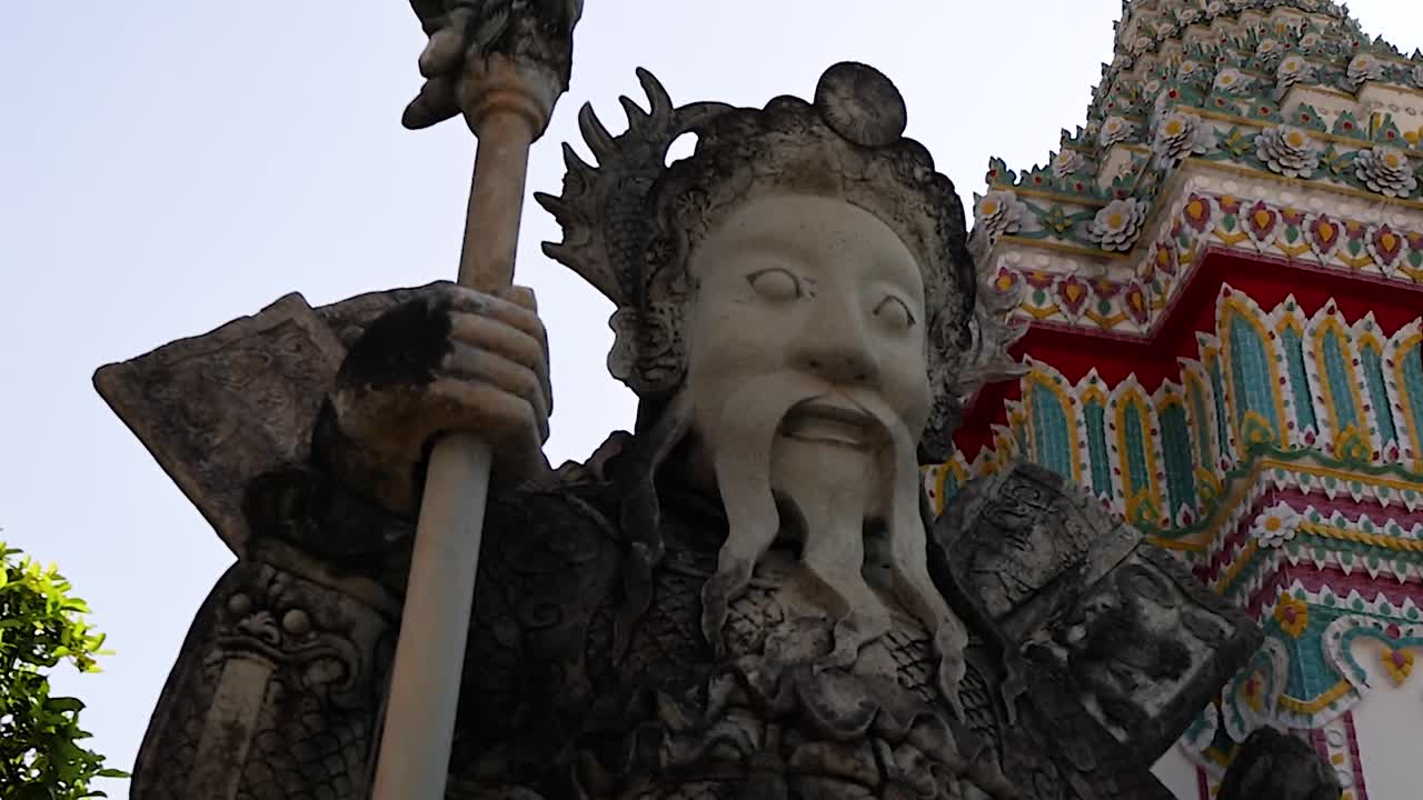 Close-up view of a detailed guardian statue with colorful temple backdrop and lush greenery.