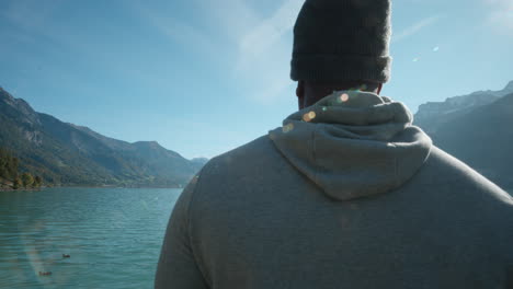 strong african american man standing quietly in deep thought as ducks pass by across beautiful lake in interlaken switzerland, europe