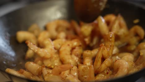 wooden spoon stirring frozen prawns inside wok