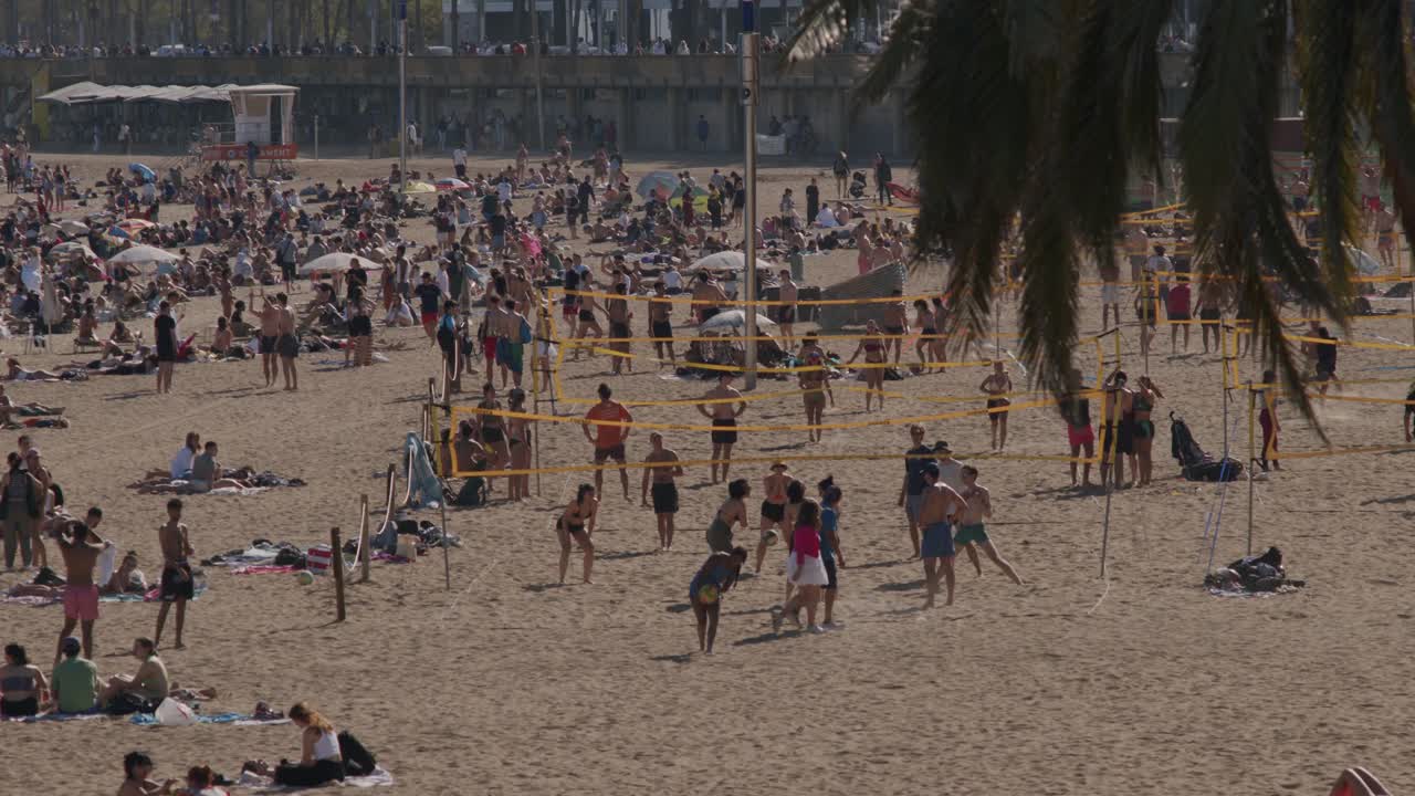Crowded Barcelona beach in summer with people sunbathing and playing volleyball