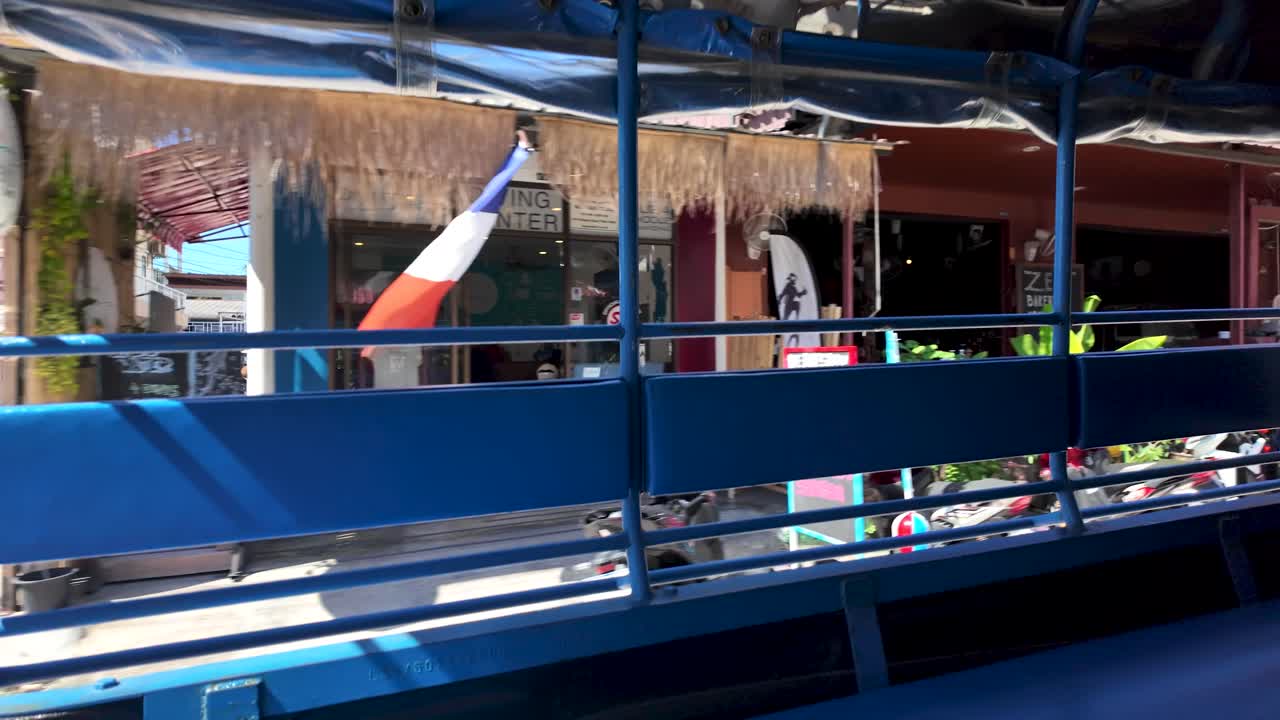 View from inside a blue songthaew in Koh Samui, Thailand, showcasing local shops and bustling street life.