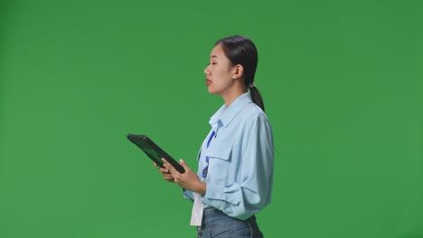 vista lateral de una mujer de negocios asiática usando una tableta mirando a su alrededor en el fondo de la pantalla verde en el estudio
