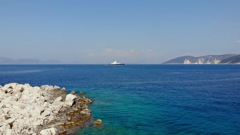 scenic rocky shoreline and blue waters of paralia emplisi, kefalonia being sailed by boats in greece with mountain slopes seen on the background- pan shot