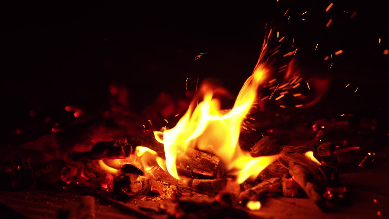 Stick hits the hot embers. Tiny numerous sparks fly up. Bonfire burning out. Close up.