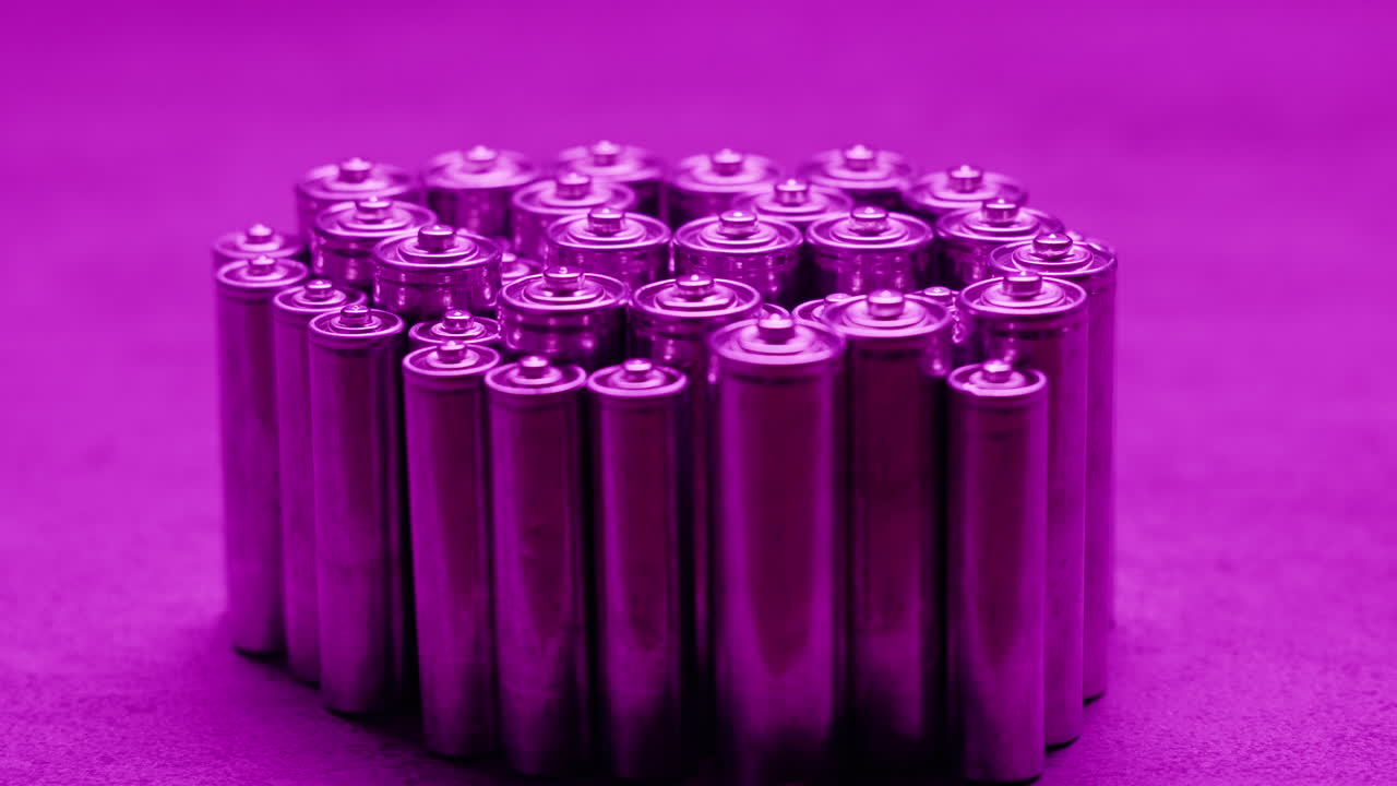 Silver batteries AA and AAA in neon light close-up. Double-A battery is a standard size single cell cylindrical dry battery. Batteries are common in portable electronic devices. An AA battery is composed of a single electrochemical cell that may be either a primary battery or a rechargeable battery.