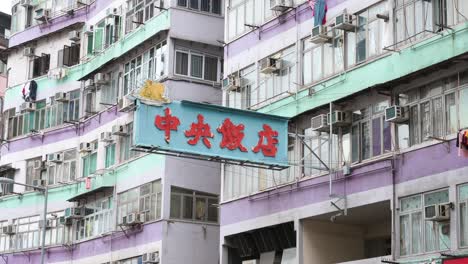 a restaurant neon sign hangs from a facade of a colorful residential building in hong kong