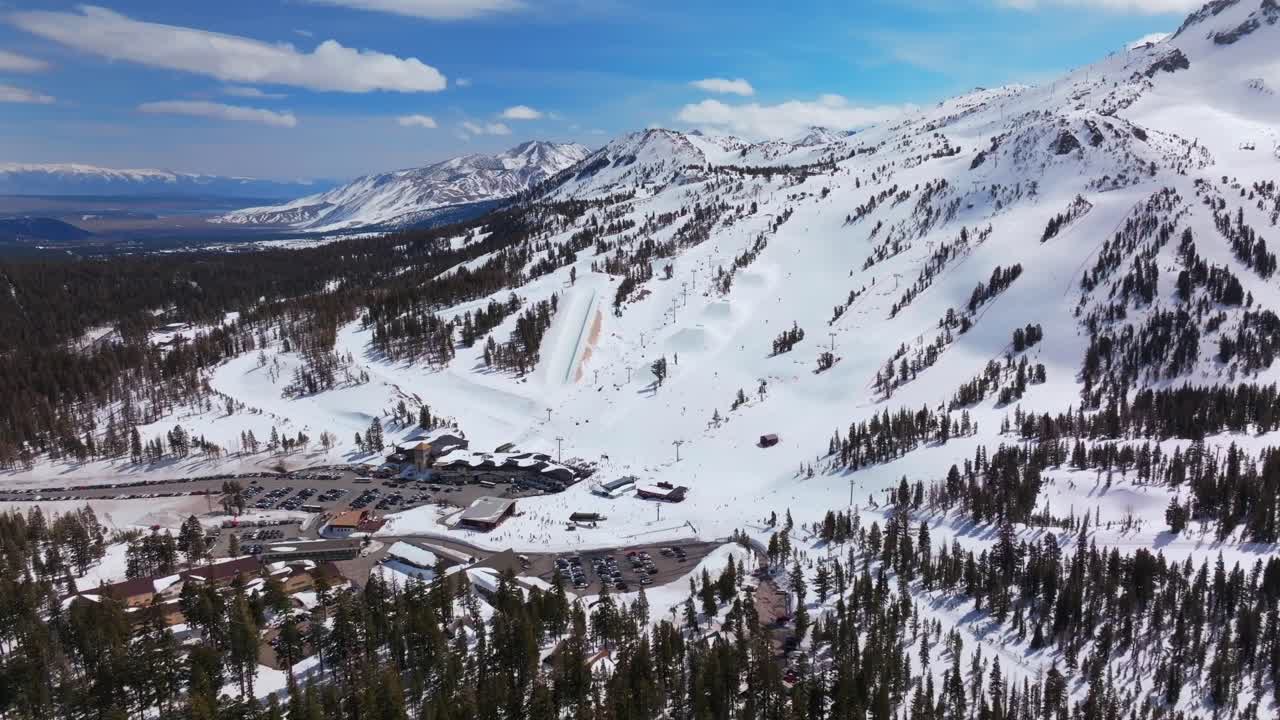 Mid winter sunny blue sky blue bird day main lodge Mammoth Mountain ski resort California aerial drone skiing snowboarding groomed trail terrain park half pipe Inyo National Forest forward down motion