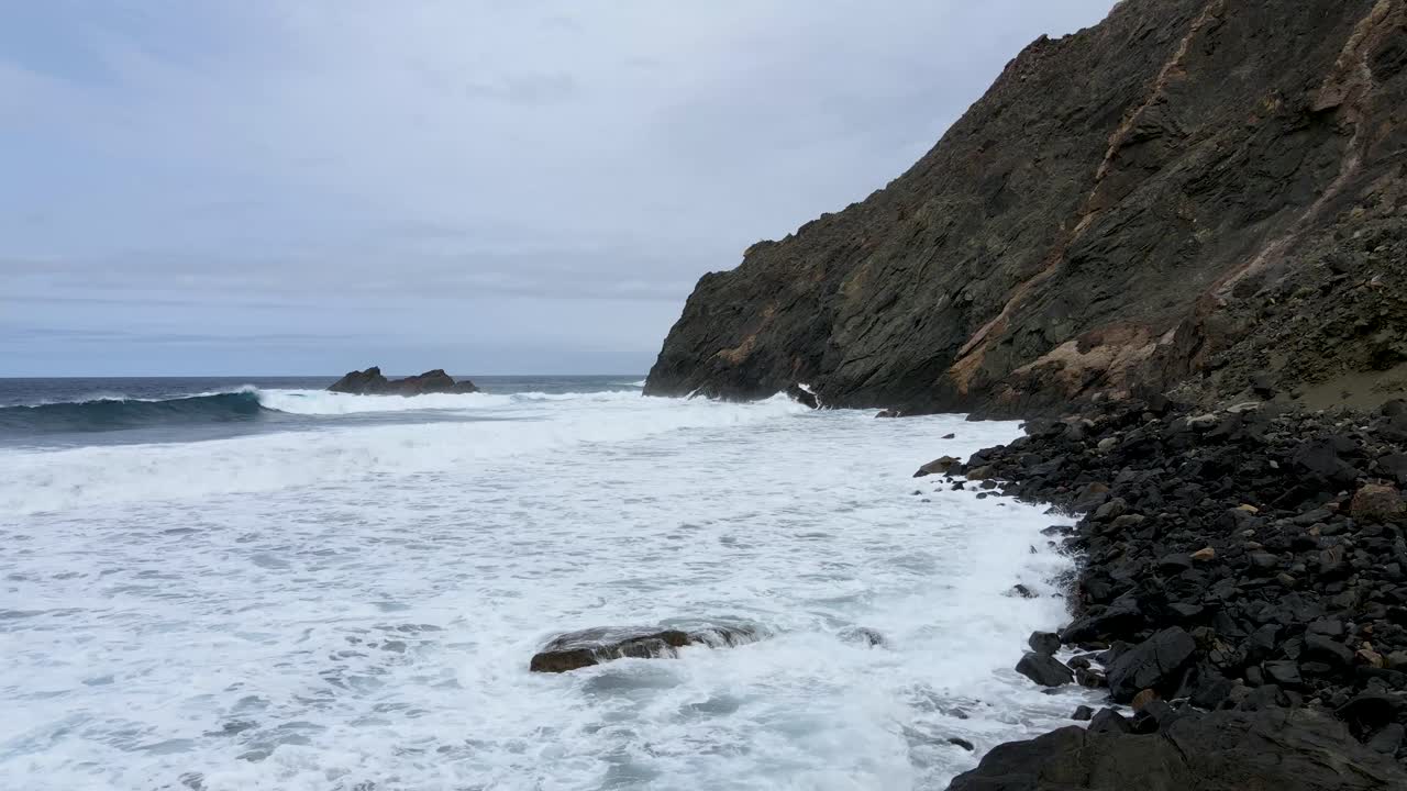 Foamy sea waves crashing into rocky beach shore in La Gomera, Canary Islands, Spain