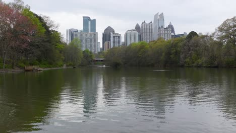 aerial push-in picturesque view of downtown atlanta skyscrapers from piedmont parks' lake clara meer on an overcast day with building reflections in the water.