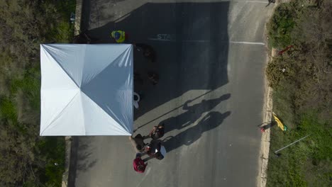 racing cars passes by the starting line of the road track on the hill in malta with tent at the side on a sunny day - aerial shot