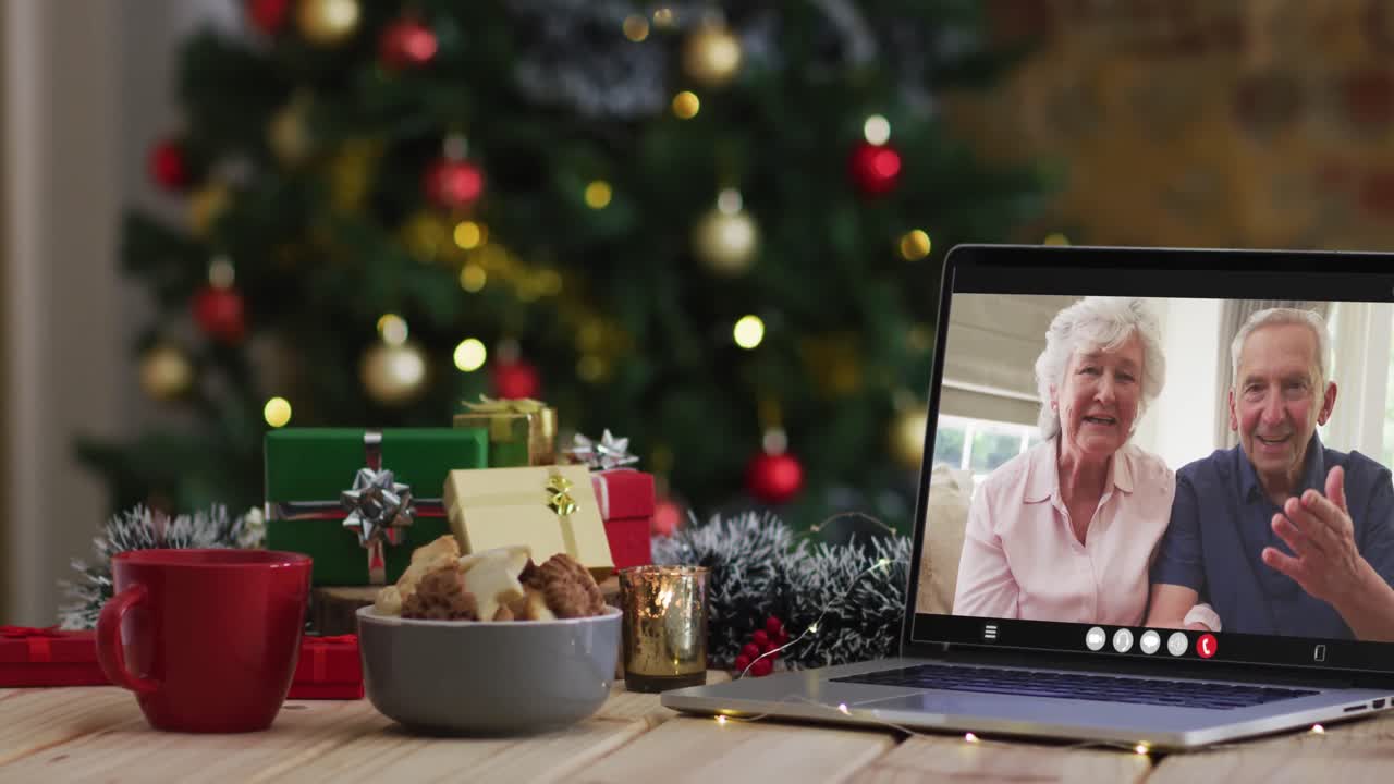 una pareja de alto nivel caucásica saludando en una videollamada en una computadora portátil, con un árbol de navidad