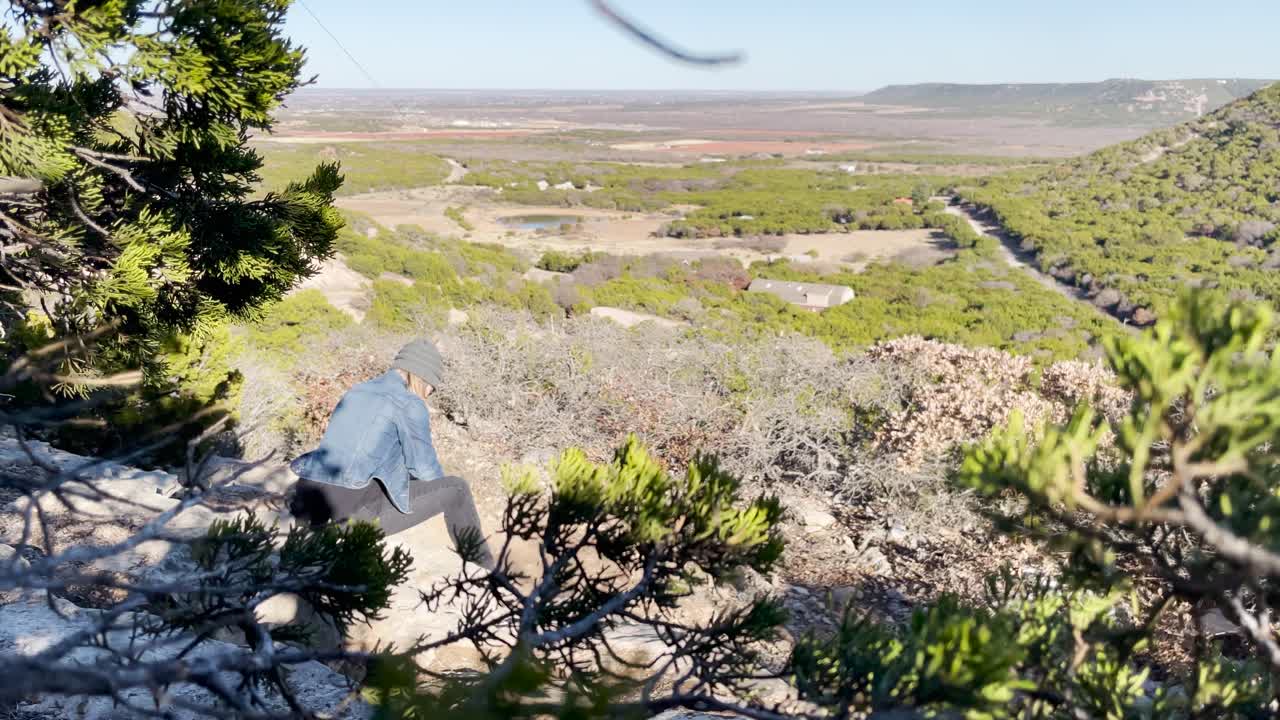 person reading a book on a cliff looking at view