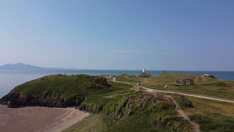 Aerial-view-across-Ynys-Llanddwyn-welsh-walking-trail-towards-Goleudy-Tŵr-Mawr-stone-lighthouse,-Anglesey