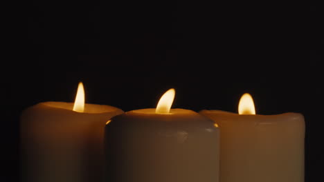 three burning candles on black background