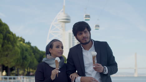 pareja árabe caminando del brazo al aire libre y comiendo helado