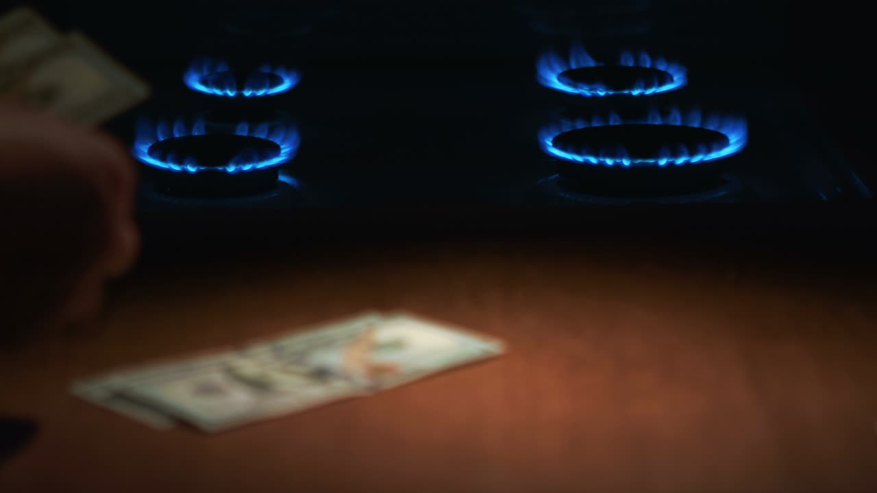 한 남자가 가스로 불타는 가스 스토브의 배경에 100달러 지폐를 세고 있습니다.