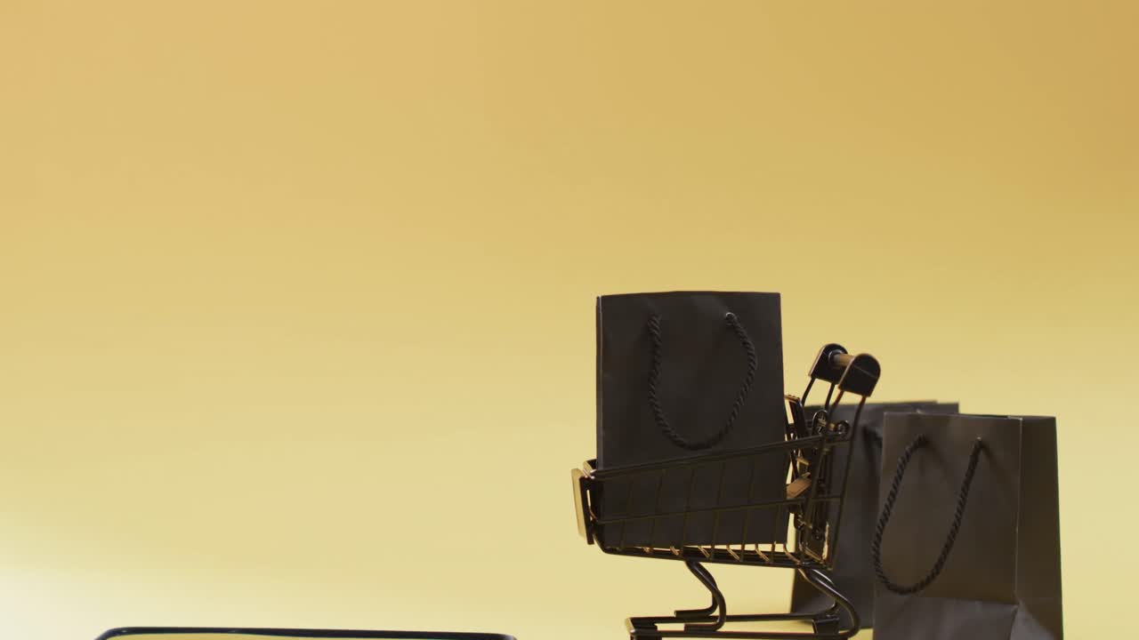 vídeo de smartphone, sacos de compras e carrinho com espaço de cópia em fundo amarelo