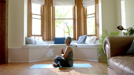 Focused-senior-biracial-woman-meditating-on-yoga-mat-at-home