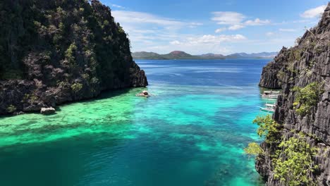 clear turquoise waters stretch between limestone cliffs at kayangan jetty and boardwalk in coron, philippines, with boats floating peacefully and a swimmer enjoying the shallow coral reef