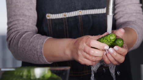 Una-Mujer-Con-Un-Delantal-Lava-Pepinos-Bajo-Un-Chorro-De-Agua-Del-Grifo-De-La-Cocina