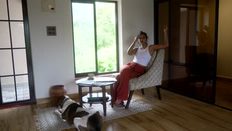 a woman in a modern living room with a dog relaxing on a rug by her side, daylight streaming in