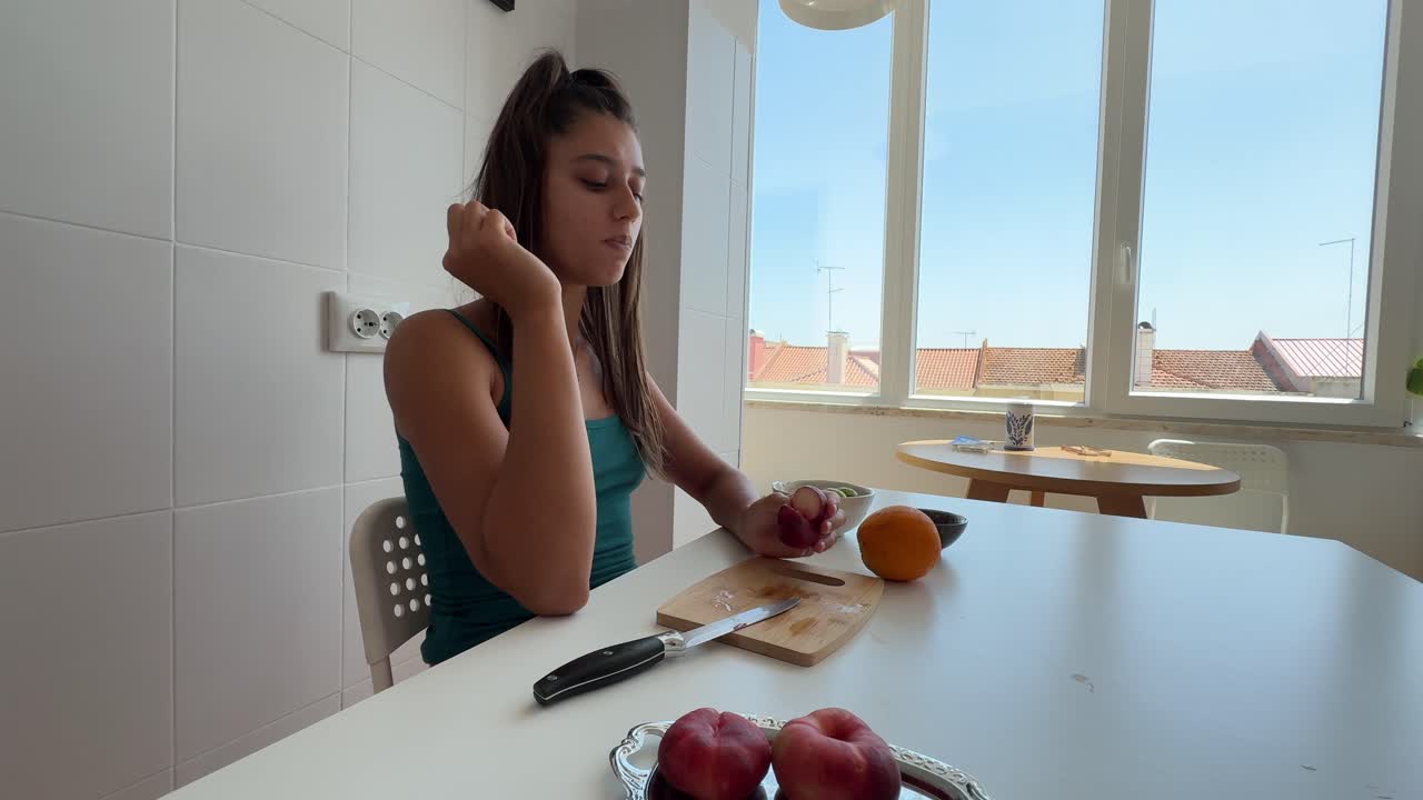 Mujer joven preparando y comiendo fruta fresca en una cocina luminosa