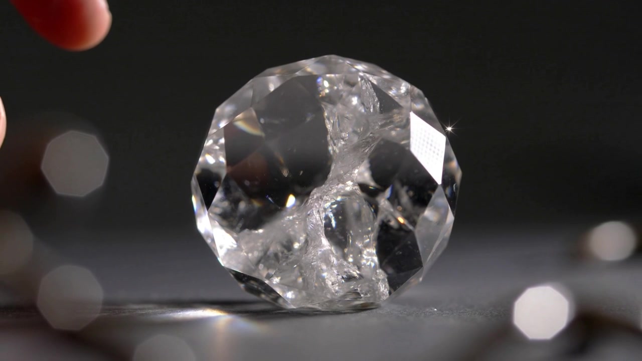 Effleurement d'un doigt d'adulte provoquant un éclat sur un cristal facetté, se retirant à mesure que l'étincelle s'estompe sur la table.