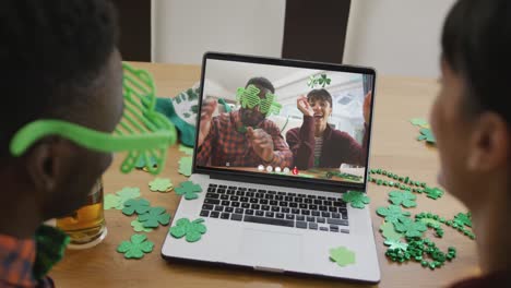 Smiling-diverse-couple-wearing-clover-shape-items-on-video-call-on-laptop