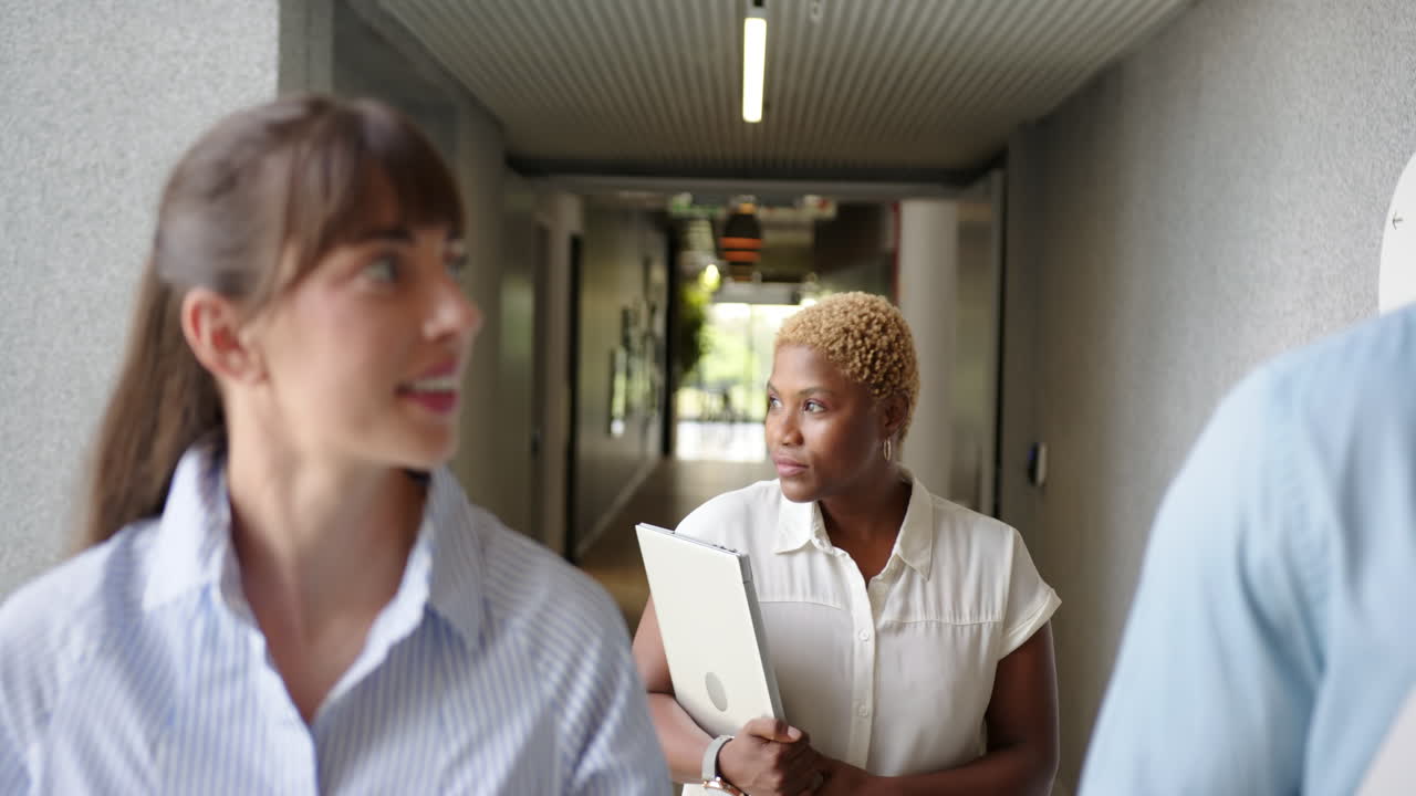 Walking in office, diverse businesswomen holding laptop and discussing work