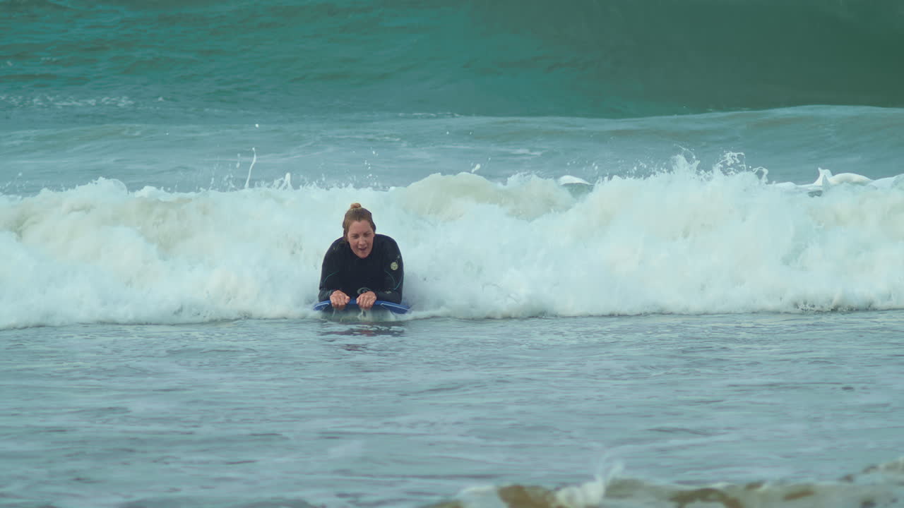 Wanita berselancar ombak dengan bodyboard di pantai, gerak lambat