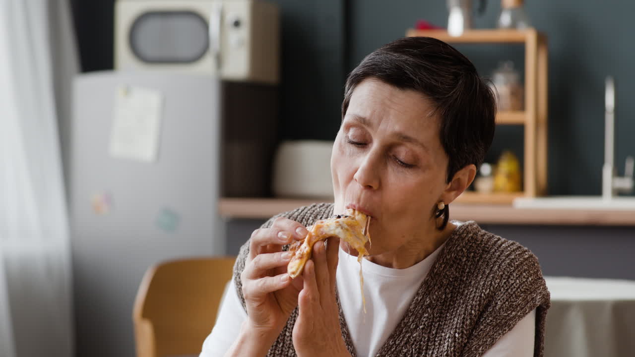 A senior woman enjoys eating a slice of pizza at home