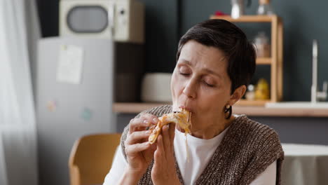 a senior woman enjoys eating a slice of pizza at home