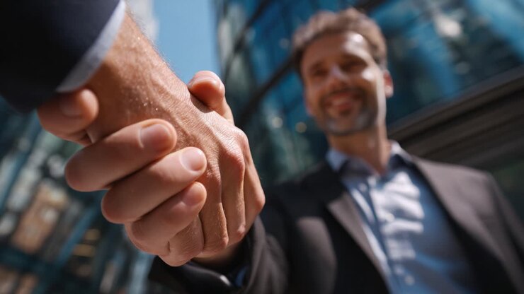 Stretta di mano professionale tra due persone che simboleggia accordo e collaborazione, sullo sfondo di un moderno contesto urbano in una giornata di sole che mette in mostra il successo aziendale e la connessione
