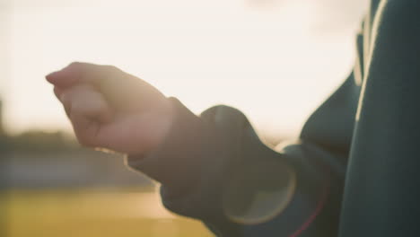 close-up of woman in green clothing performing wrist twist with blurred background featuring greenery, capturing the hand movement with sunlight creating a soft glow in the outdoor setting