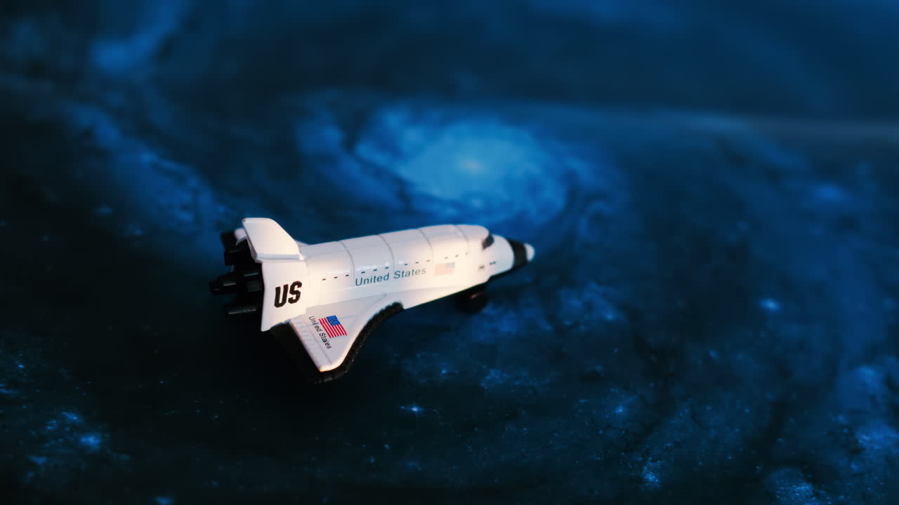 Close up of a miniature toy space shuttle placed on a blue cosmic galaxy backdrop