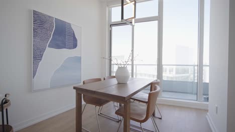 Pan-and-dolly-shot-of-the-dining-area-in-a-high-ceiling-penthouse-condominium-unit-with-a-floor-to-ceiling-window-wall-at-the-back-and-balcony-outside-during-a-sunny-day