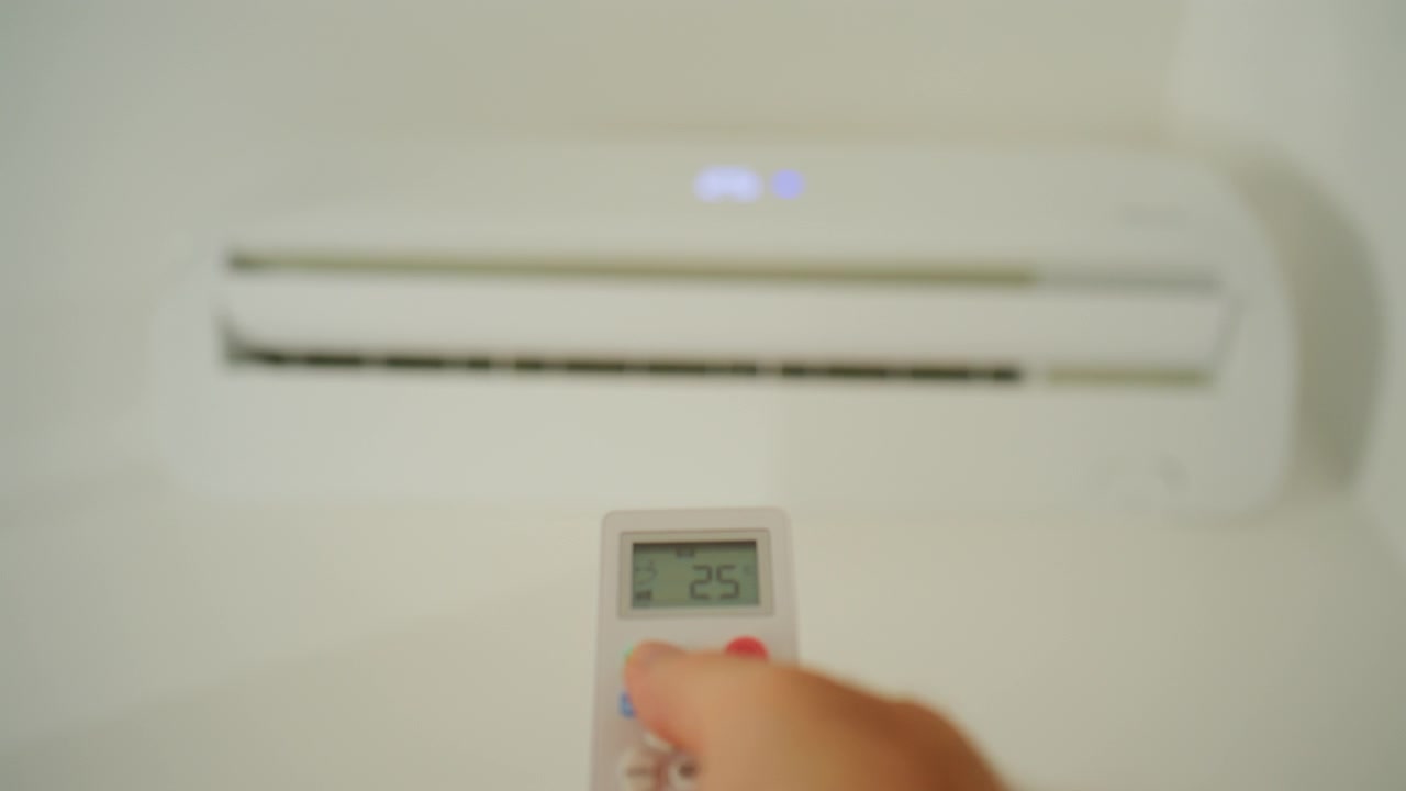 Hand die een afstandsbediening vasthoudt, de temperatuur aanpassend op een moderne airconditioningunit voor optimale klimaatbeheersing en comfort.