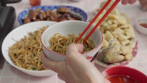 serving chinese noodles in bowl using chopsticks, asian food and fried fish on table