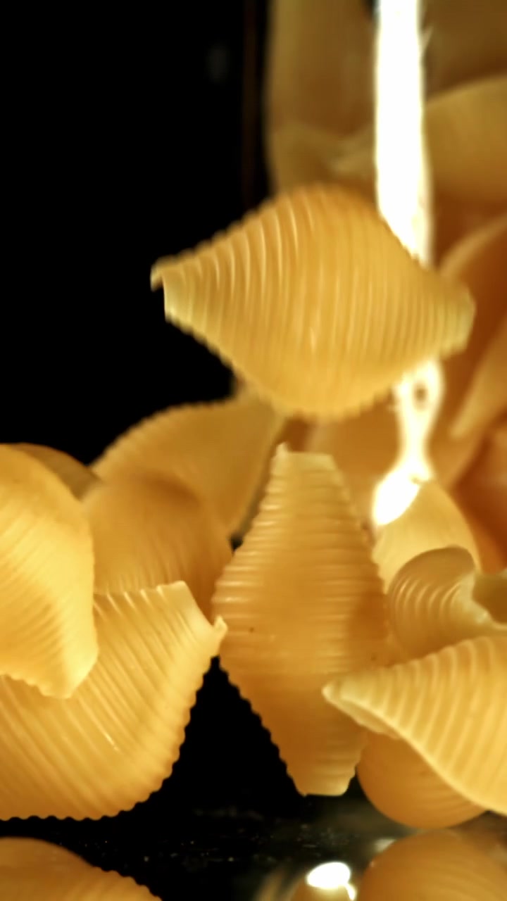 Pasta conchiglie cruda che cade al rallentatore su sfondo nero