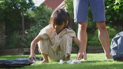 asian daughter having fun in garden helping father to put up tent for summer camping trip together