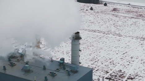 Chimeneas-Industriales-Que-Emiten-Vapor-Contra-Un-Paisaje-Nevado,-Clima-Nublado,-Vista-Aérea