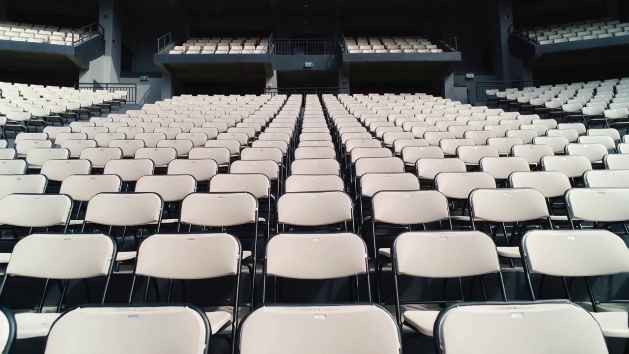 Registrazione avviata, telecamera di rilevamento che avanza nell'arena, documentando sedie pieghevoli beige