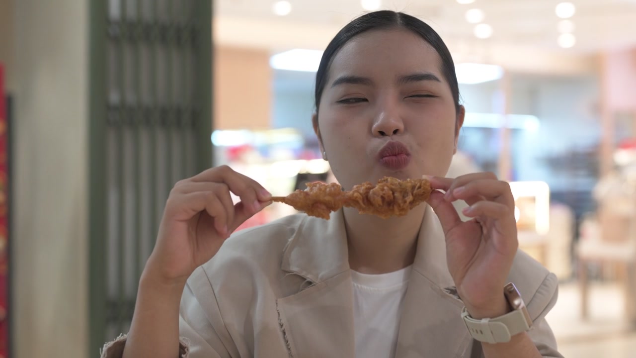 Pengusaha wanita muda Thai Isan yang lapar sedang makan sate ayam goreng di meja pujasera
