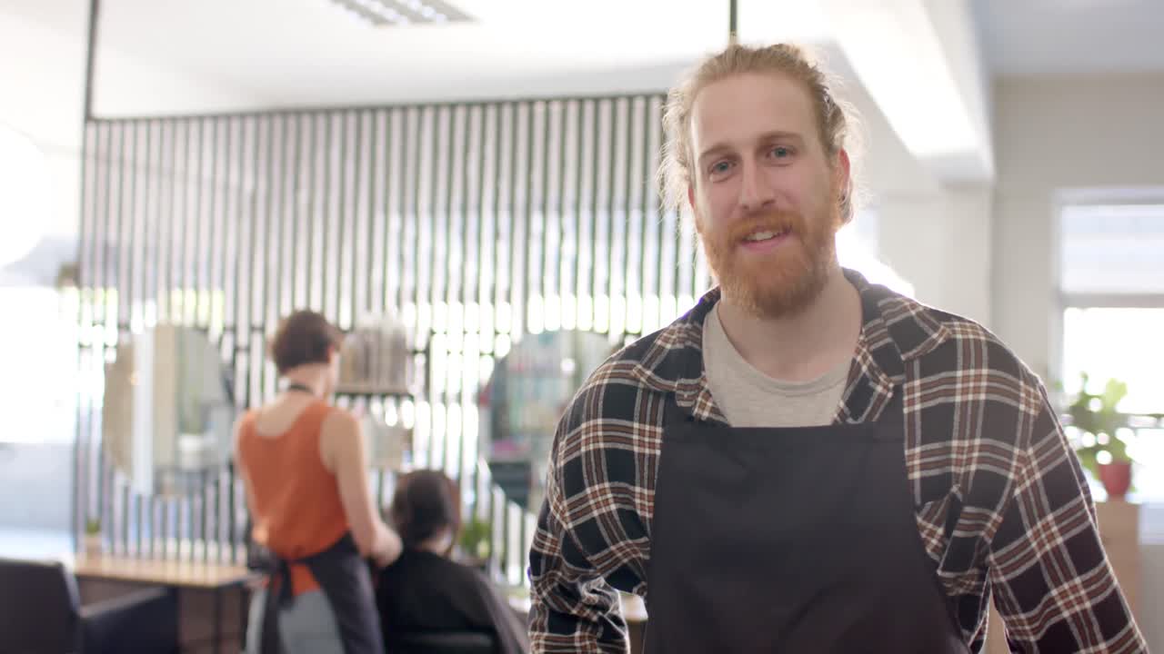 Porträt eines lächelnden kaukasischen Friseurs mit Schürze in einem Friseursalon, mit Platz für Text, in Zeitlupe.
